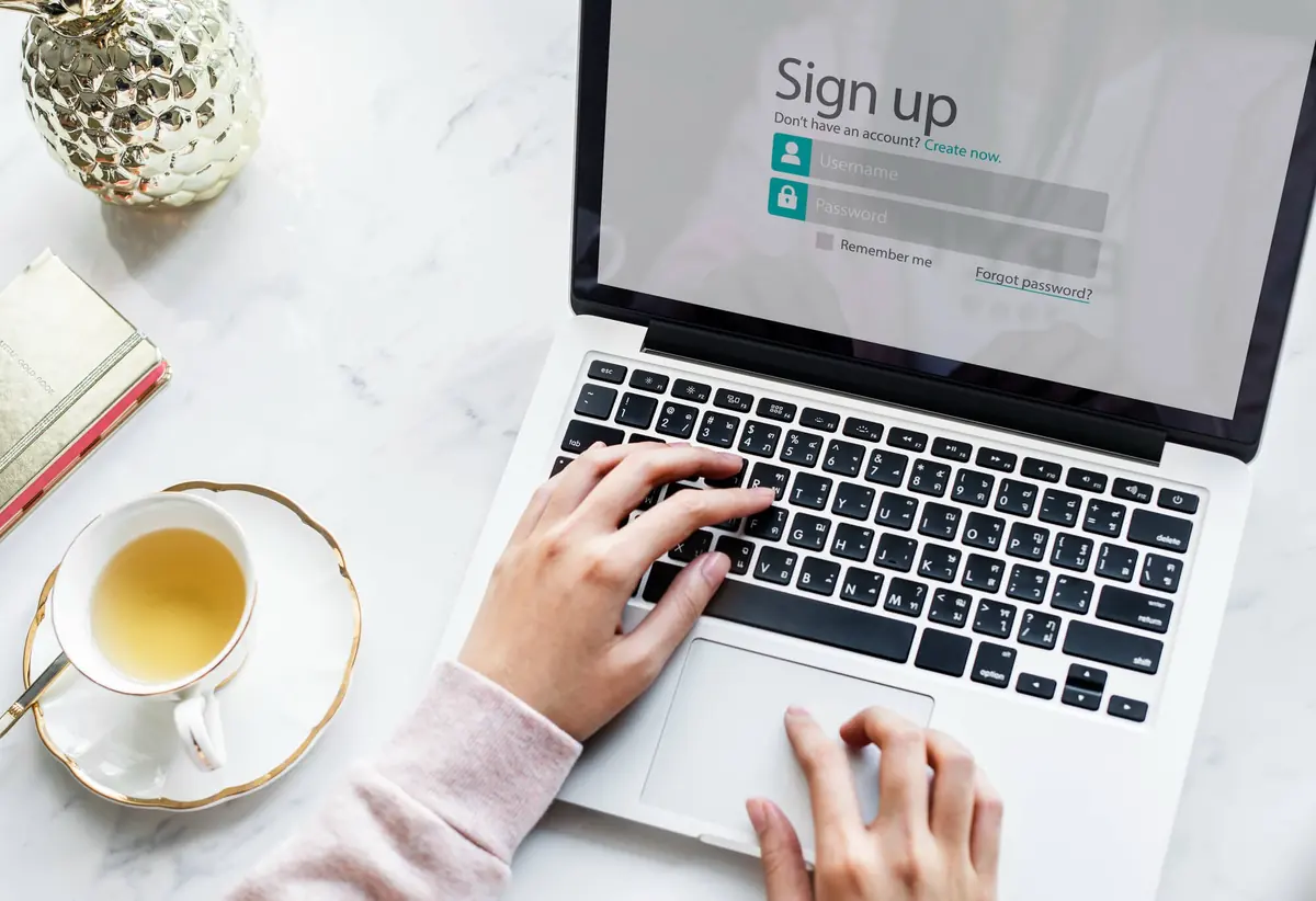 Someone filling in a sign-up form on a laptop beside a cup of tea